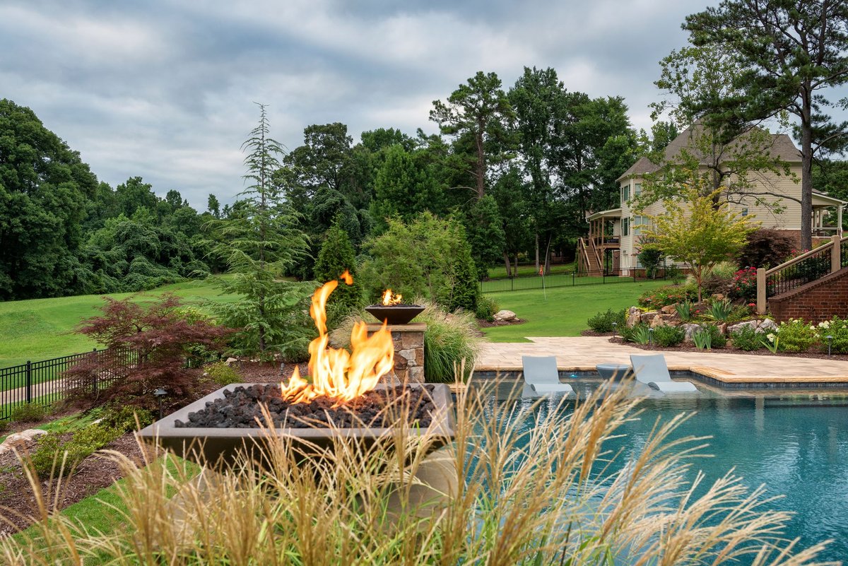 Fire feature burning at the pool's edge framed by ornamental grasses, Traditions of Braselton, Jefferson GA